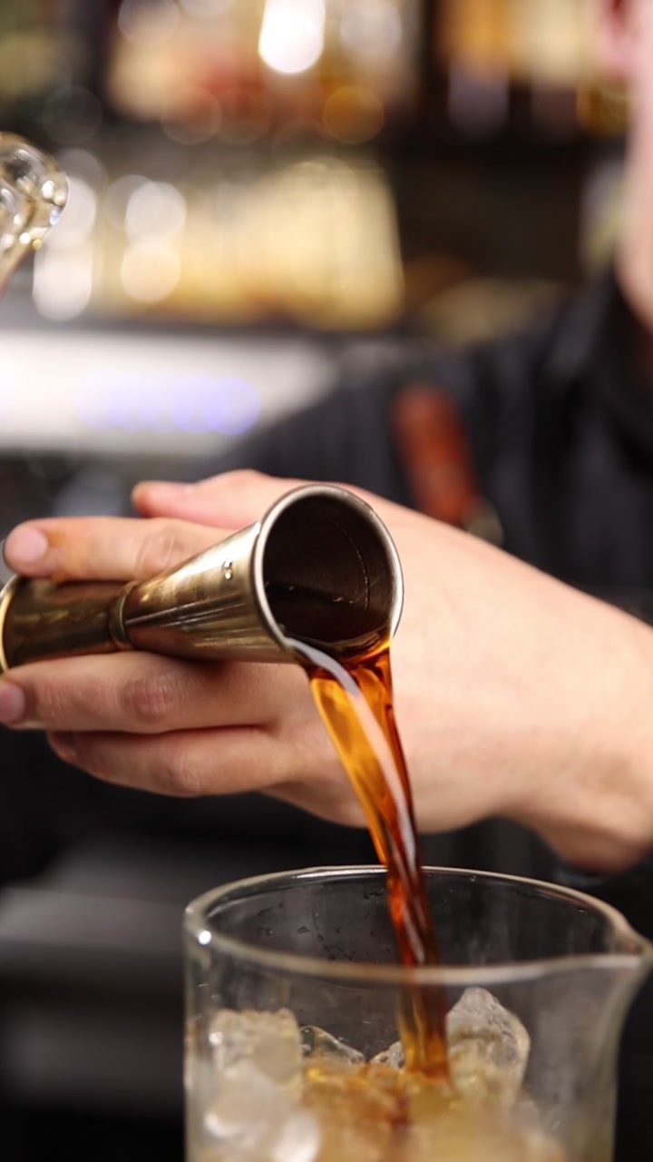 Barman che versa alcol da una bottiglia in un jigger e un bicchiere