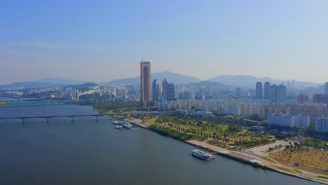 drone shot traveling forward and downward above the han river toward a business district and a park in seoul city during the day