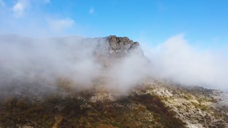 Toma-De-Un-Dron-De-Un-Pico-De-Montaña-Cubierto-De-Niebla-En-Un-Día-Soleado-De-Otoño-Con-Cielo-Azul