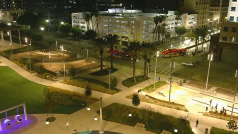 Aerial-rising-shot-of-Lincoln-Park-in-downtown-Long-Beach-|-Night-time-|-Palm-trees-and-city-bus-in-background