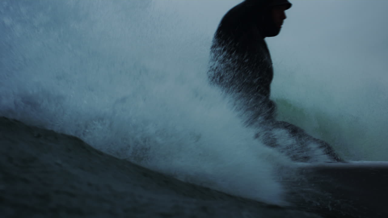 In water view of surfer riding through stormy conditions as they bend and cut back and spray in cold atlantic ocean water
