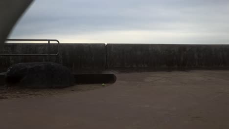 camera moves between two whale tail shaped benches to rise above wall and display the choppy ocean on the far side