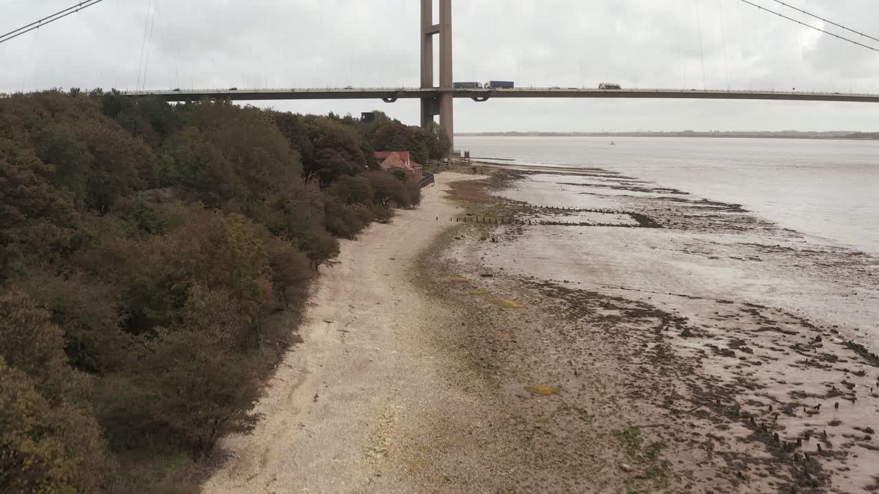 una fotografía aérea de una costa desierta que corre bajo un gran puente colgante con coches, camiones y una autopista a su lado