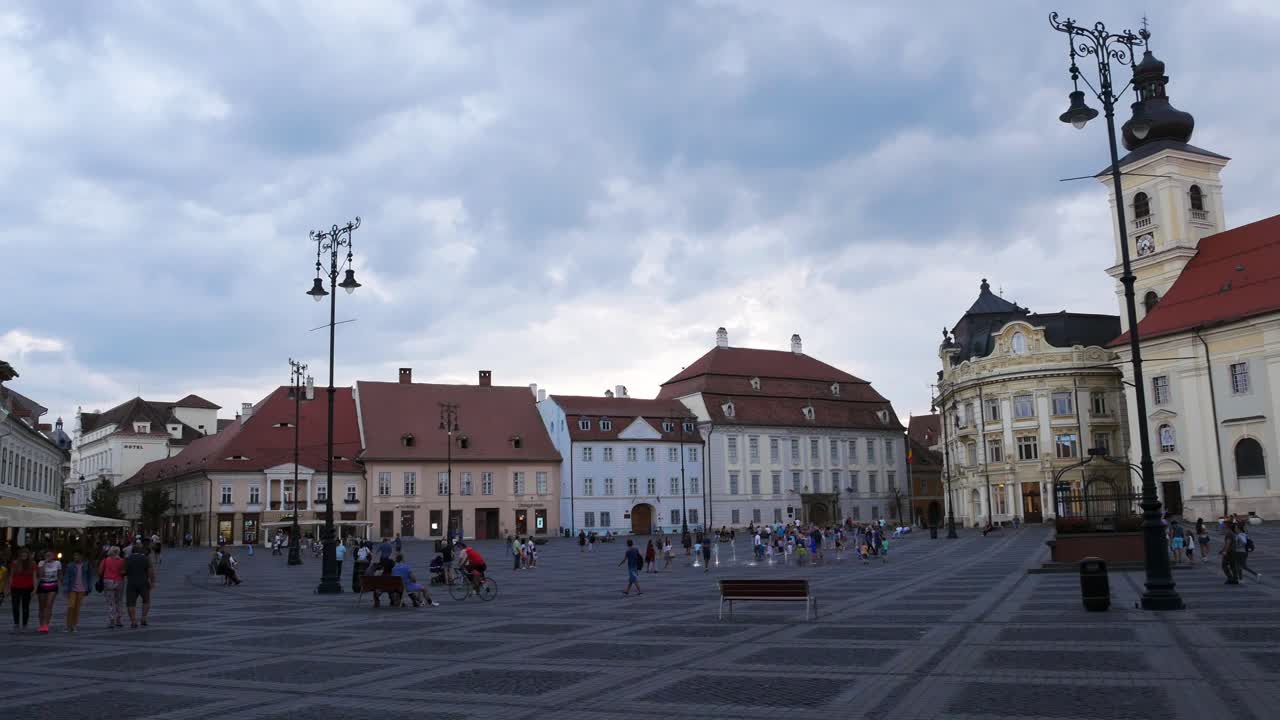 Panning shot of Mare square (Piata Mare) in Sibiu, Romania, on a cloudy summer evening. Tourists and locals enjoying the warm temperature.