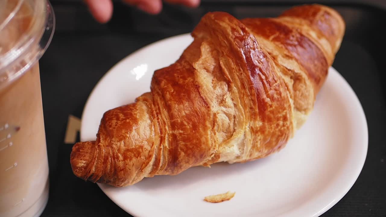 Mano che afferra un croissant dorato con caffè
