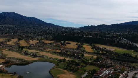 Dron-Panorámico-A-La-Izquierda-Y-Luego-Hacia-Abajo,-Pasando-De-La-Toma-De-Las-Montañas-A-Una-Vista-Asombrosa-De-La-Fuente-Y-El-Lago-Del-Campo-De-Golf