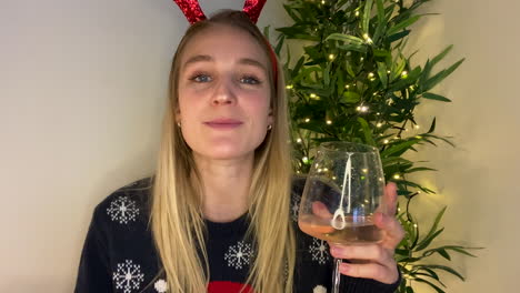 young woman on christmas video call playfully raising her glass to camera