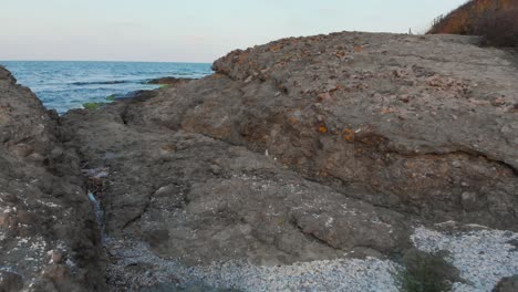 Sehr-Niedrige-Luftaufnahme,-Dron-Passiert-Zwischen-Küstenfelsen-Und-Kommt-über-Das-Meer-Heraus