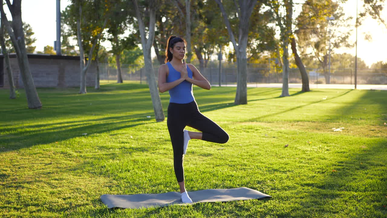 una hermosa joven yogui riéndose mientras se cae y pierde el equilibrio en una pose de yoga con manos de oración de una sola pierna en el parque al amanecer.