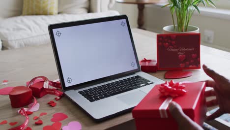 Midsection-of-biracial-man-holding-present-and-having-valentine's-video-call-on-laptop