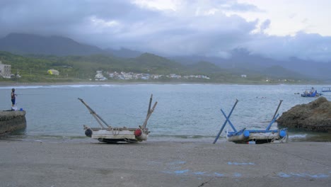 fisherman and beached rafts at a boat ramp with mountains and cloudy sky in background, filmed in wide as establishing shot