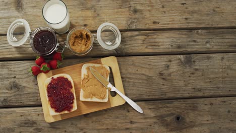 peanut butter and jelly sandwich on wooden tray with milk and strawberries on wooden surface