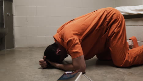 a sad, depressed man in orange prison uniform laying on prison cell floor weeping, crying, praying