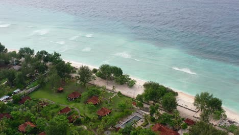 tropical white sand beach on gili trawangan island with turquoise waves crashing at sunset, aerial