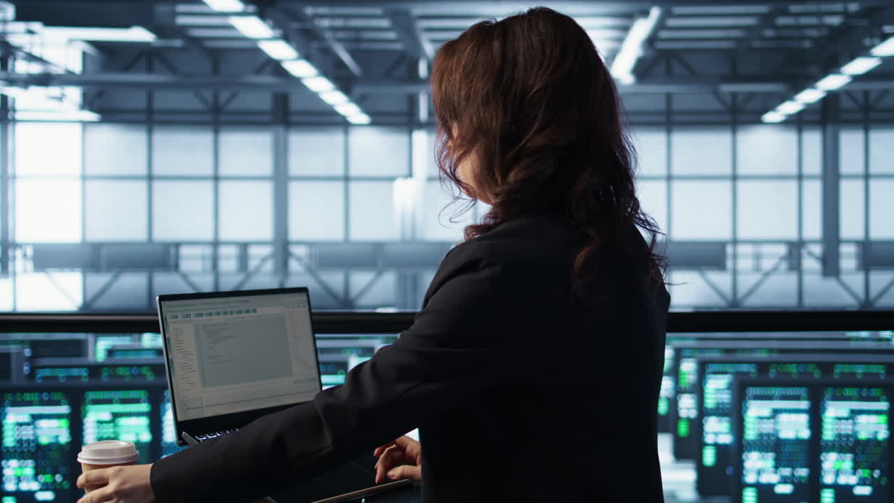 Woman in data center using laptop to update storage arrays, holding coffee cup