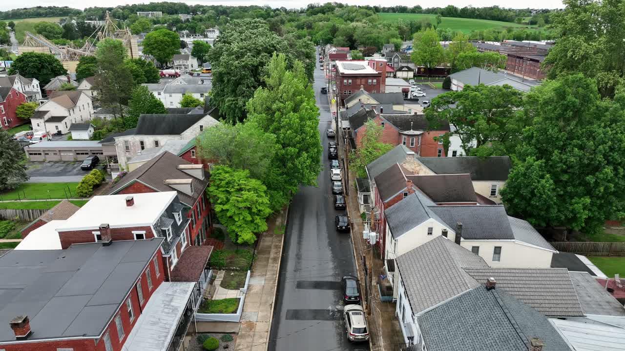 Blowing American flag on street of neighborhood with historic homes. Aerial tilt up wide shot. Colored houses in peaceful housing area of PA, United States. Rainy spring day.