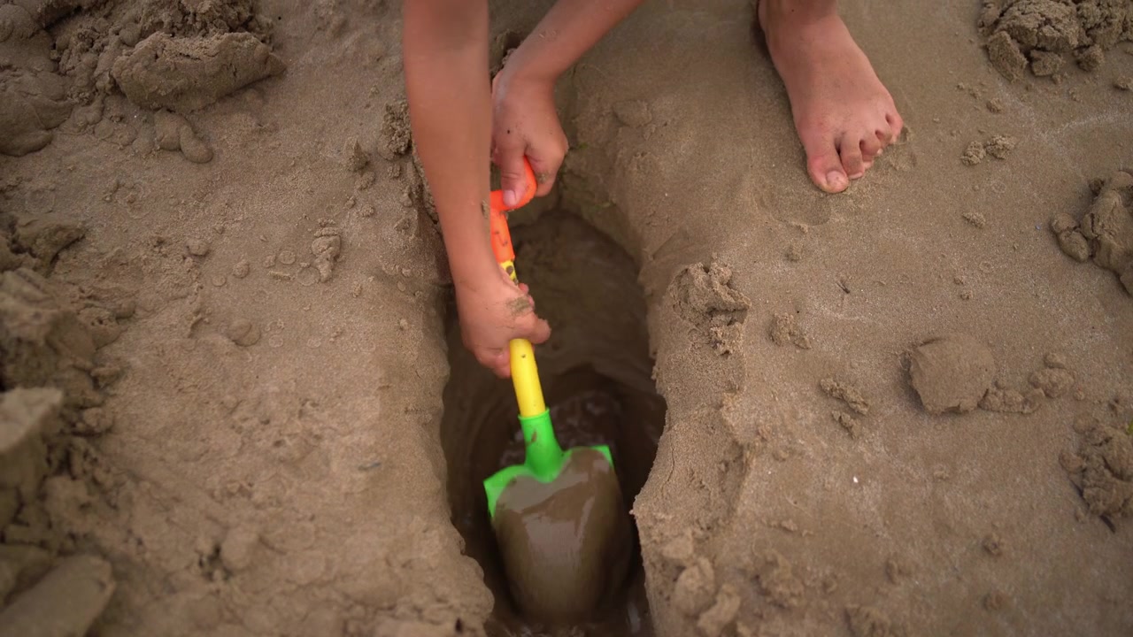 Close-up of a boy scooping sand from a hole filled with water using a small shovel