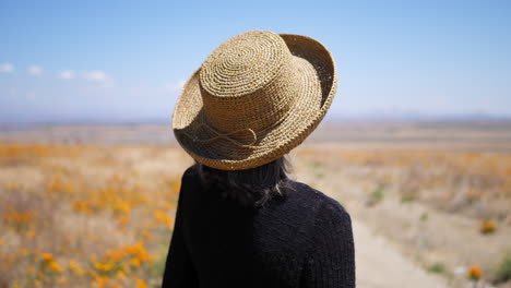 una anciana en un camino de tierra hablando y gesticulando con las manos en un campo de flores naranjas a cámara lenta