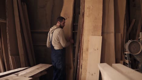 a worker in a carpentry workshop full of timber chooses the suitable material for work