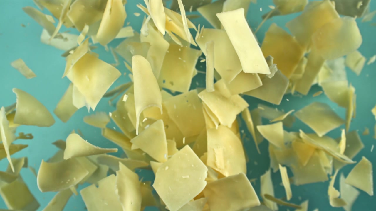 Scaglie di Parmigiano in caduta al rallentatore su sfondo blu