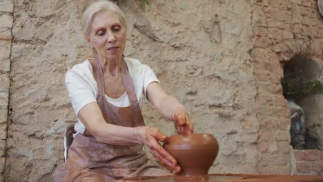 una mujer anciana alfarera en un delantal hace una olla en un taller de cerámica