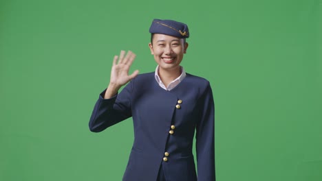 asian woman air hostess smiling, waving hand, and saying bye while standing in the green screen background studio