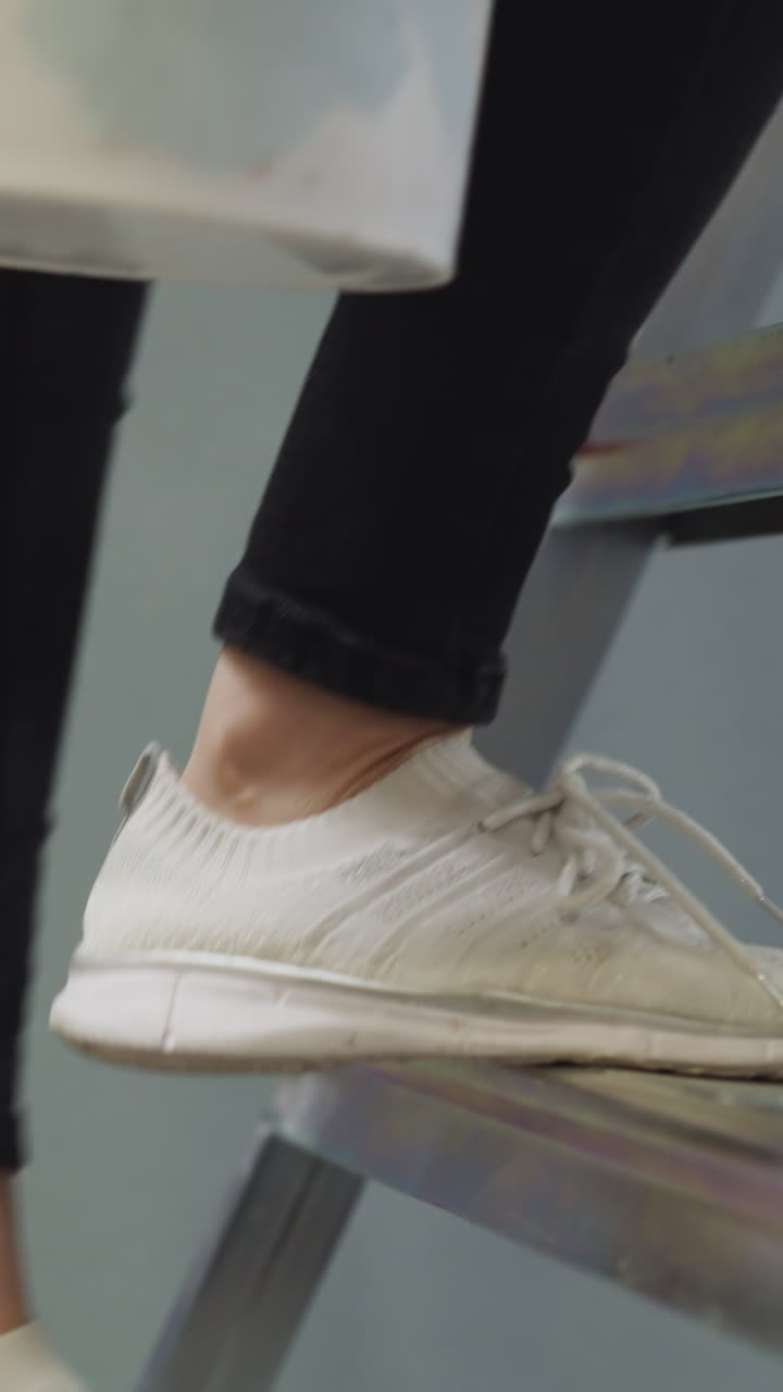 Lady goes up step ladder holding paint bucket in light room closeup. Person does repair in house by herself. Woman ready to paint walls at home