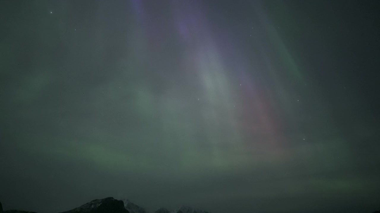 Vibrante Aurora Boreale che danza su un paesaggio montano innevato