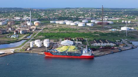 Large-pile-of-sulfur-offloaded-from-transport-boat-at-dock-with-oil-refinery-flare-stacks-behind