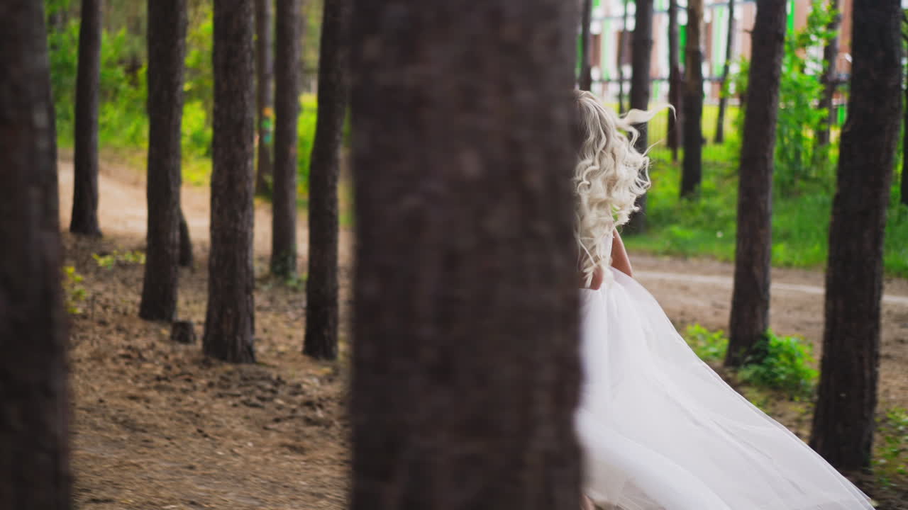 Attractive curly haired lady bride runs along pine forest