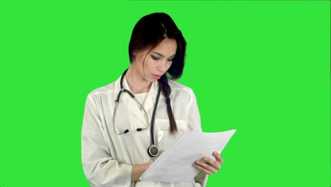 young female doctor reading patient medical history forms on a green screen, chroma key