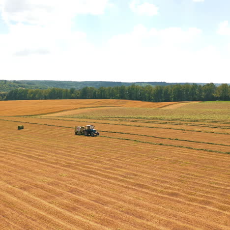 aerial view on the field and tractor working on the natural rural background. flight over agricultural field during grass harvest for livestock.