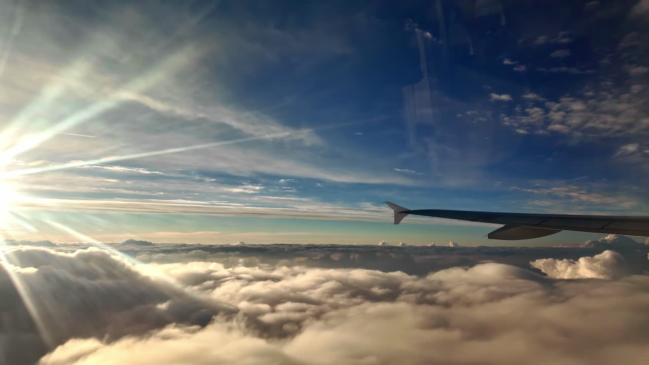 Airplane wing view above clouds with bright sunlight and a vast blue sky