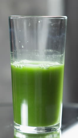 vaso medio lleno de jugo verde con luz de fondo natural y detalles de burbujas