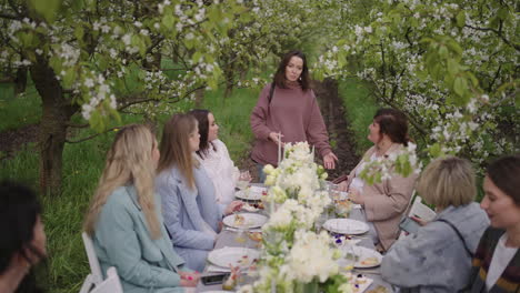 Amigos-Y-Familiares-Reunidos-En-El-Jardín,-La-Gente-Está-Almorzando-En-Un-Huerto-Floreciente-En-Primavera