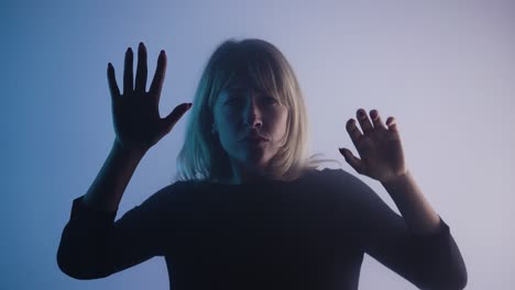 young woman appears from smoke mysteriously looks into camera and touches glass with her palms