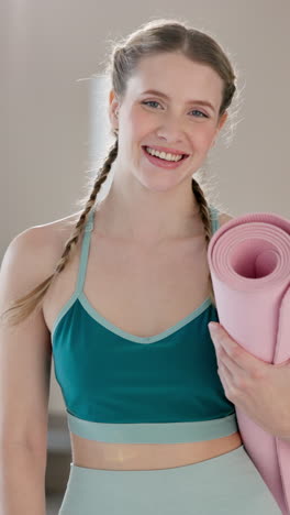 woman in a green sports bra and braids smiling with a yoga mat