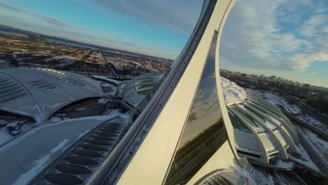 fpv drone flies over montreal’s snow-covered olympic stadium at sunset, winter setting in canada