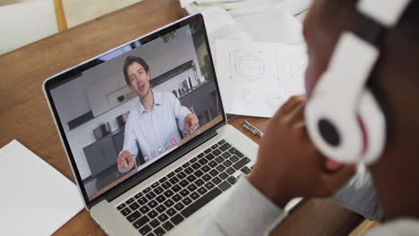 estudiante universitario afroamericano que sostiene notas mientras hace una videollamada en una computadora portátil en casa