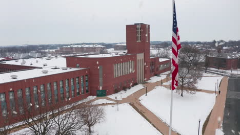 Aerial establishing shot of large brick school during snowstorm