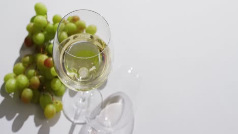 white wine glass and grapes lying on white surface with copy space