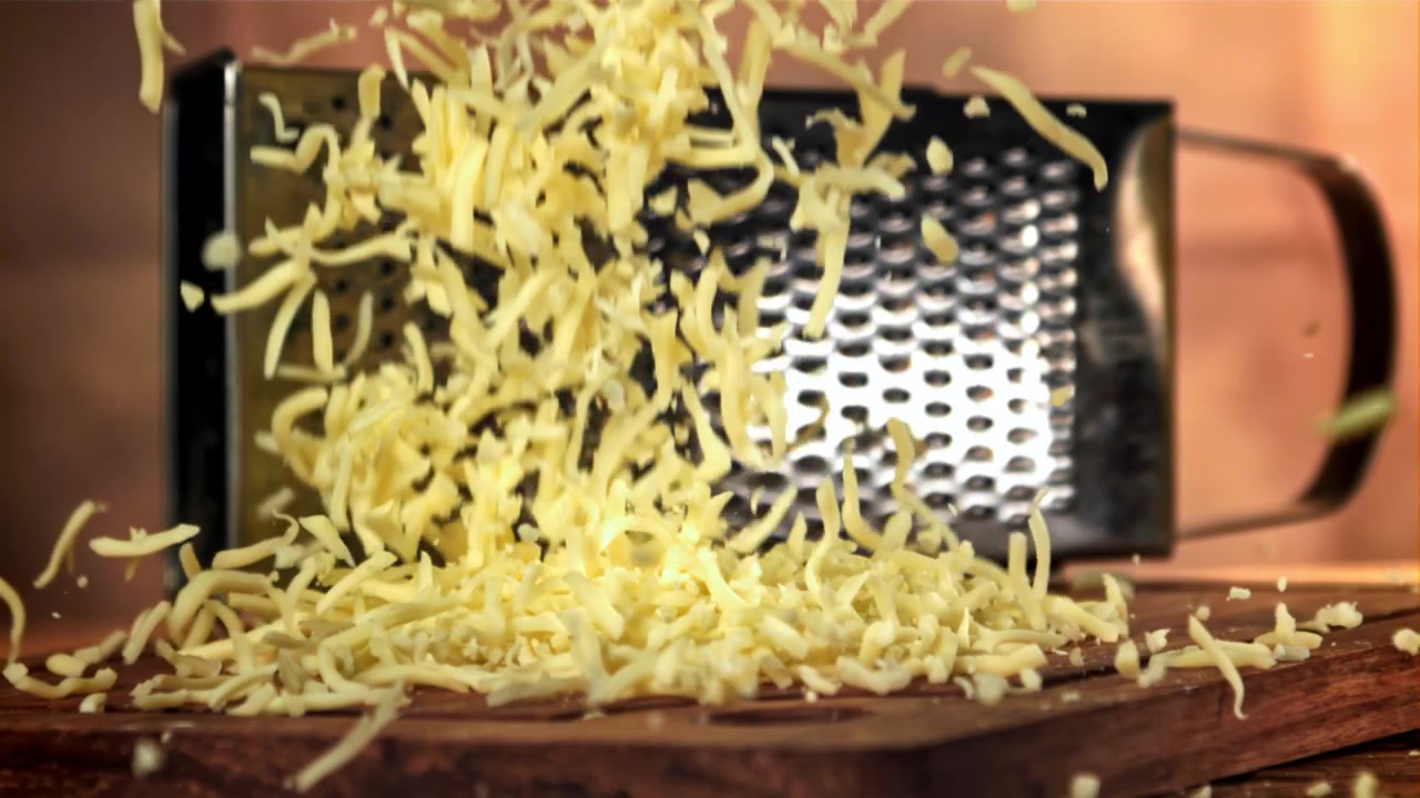 Formaggio grattugiato che cade su un tagliere di legno al rallentatore