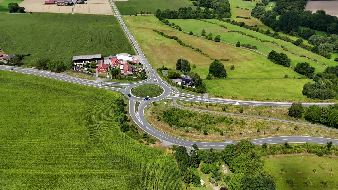 Driving cars on new roundabout in rural farm area of American town. Aerial lateral wide shot. Sunny day with green grass and pastures in countryside. Quiet and peaceful landscape of USA
