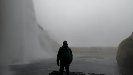 cinematic shot behind the icelandic waterfall seljalandsfoss and where a man admires the beauty and strength of the falling water