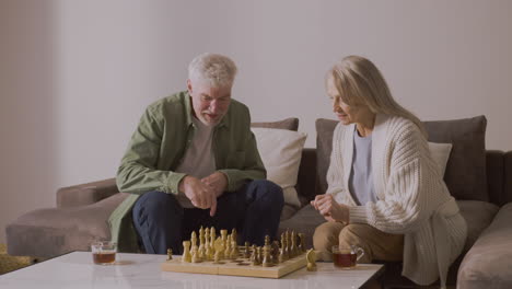 senior man and woman playing chess while sitting on sofa at home