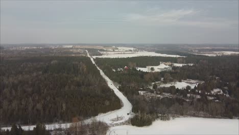 Luftaufnahme-Eines-Autos,-Das-Im-Winter-Auf-Einer-Schneebedeckten-Straße-Fährt,-Die-Von-Wald-Umgeben-Ist