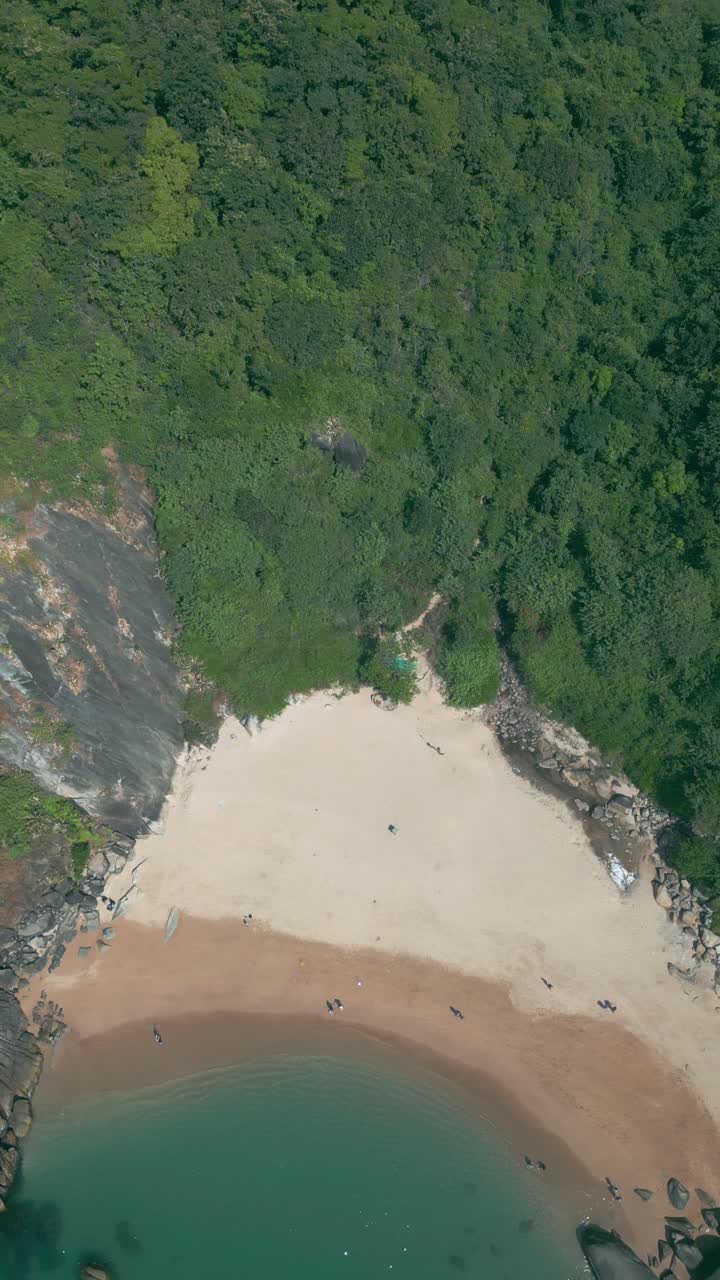 A stunning aerial top view of Butterfly Beach, Goa, featuring golden sands and clear waters. People relax and enjoy the serene beach, while lush green hills create a breathtaking natural backdrop