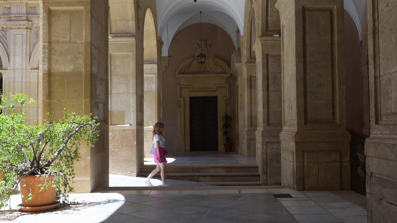 Ragazza che cammina al rallentatore attraverso un chiostro storico con eleganti archi in pietra a Murcia, Spagna