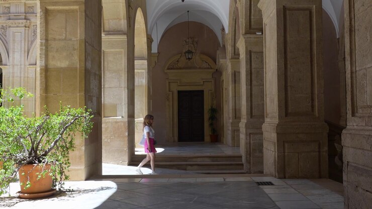 Ragazza che cammina al rallentatore attraverso un chiostro storico con eleganti archi in pietra a Murcia, Spagna