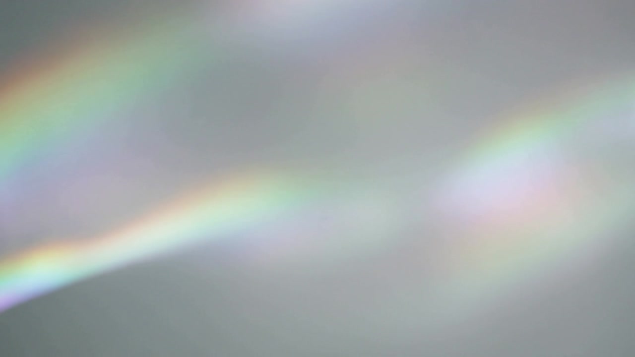Forming streak iridescent light bands shifting across gray backdrop by refraction with soft patches